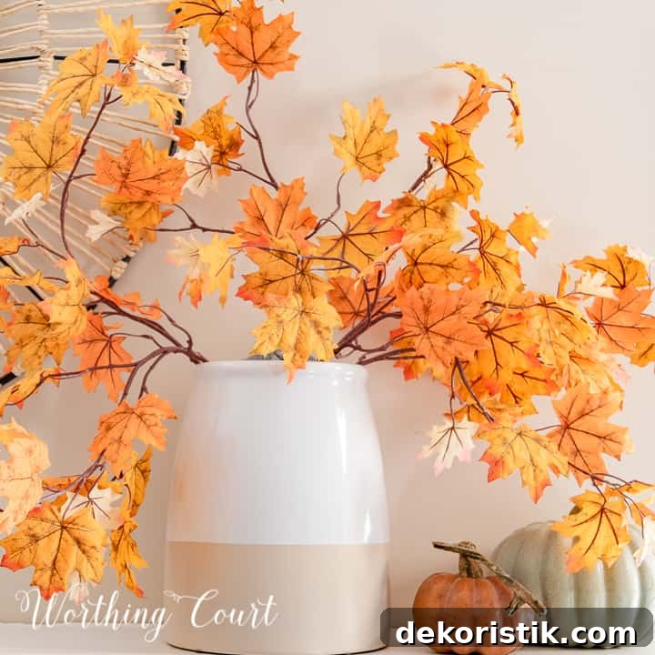 vase with fall leaf stems and two faux pumpkins on a white mantel