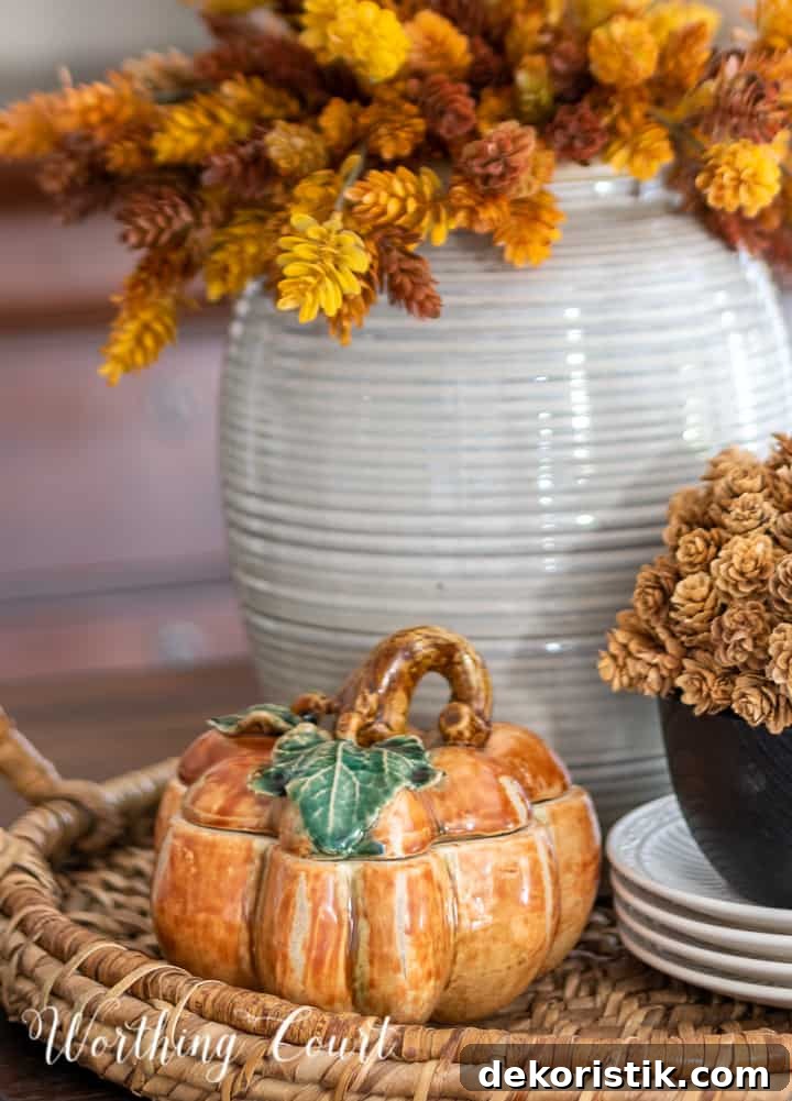 fall centerpiece in a woven tray with a containers filled with faux fall stems and a ceramic pumpkin box