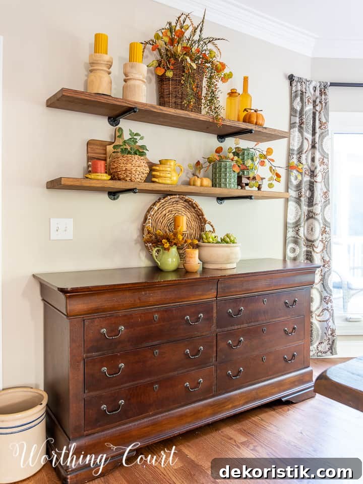 wooden open shelves above a sideboard decorated for fall with rich amber and green accessories