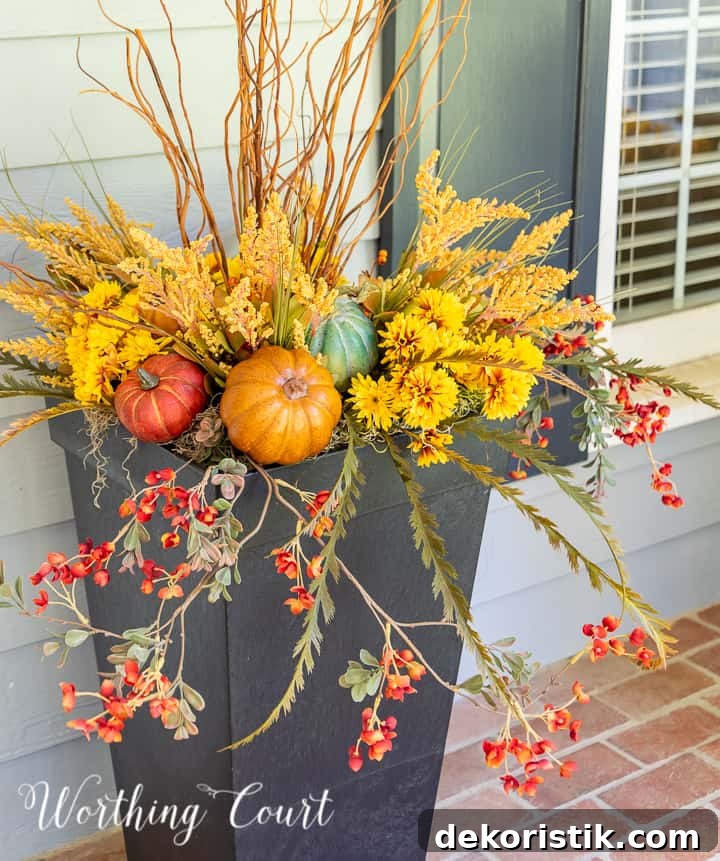 natural sticks, faux golden mums and multi colored pumpkins in a tall black urn