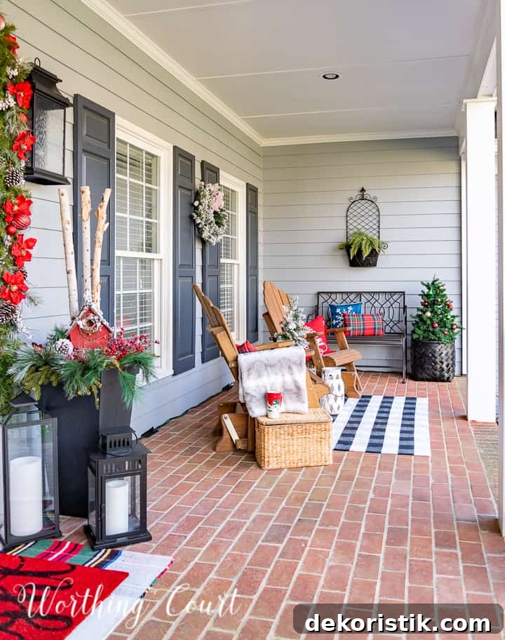front porch decorated for Christmas with red and white garland, planters, trees, lanterns, rugs and pillows