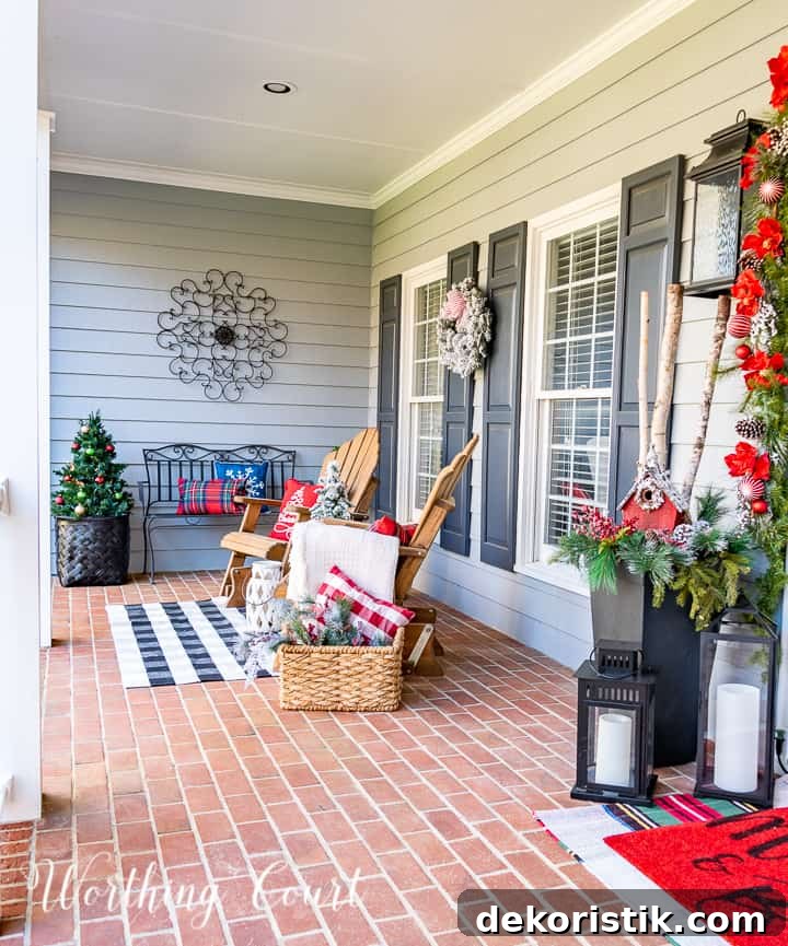 front porch decorated for Christmas with red and white garland, planters, trees, lanterns, rugs and pillows