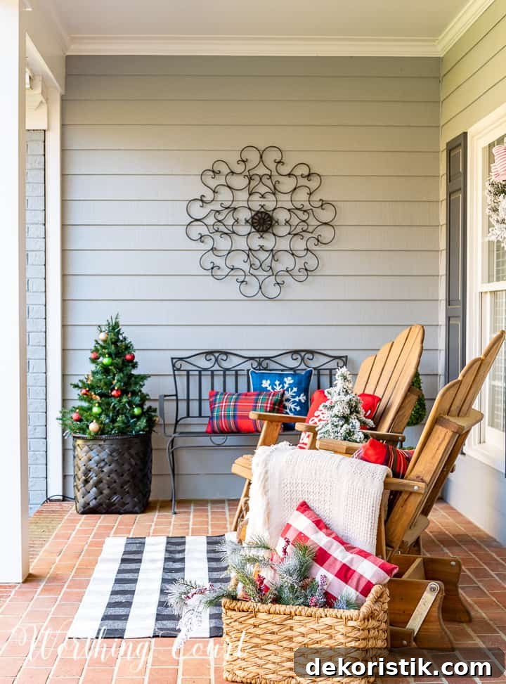 front porch decorated for Christmas with red and white garland, planters, trees, lanterns, rugs and pillows
