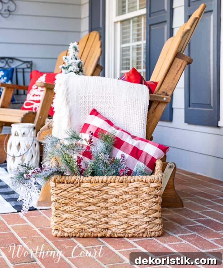front porch decorated for Christmas with red and white garland, planters, trees, lanterns, rugs and pillows