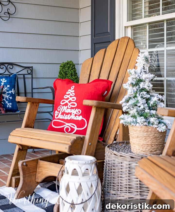 front porch decorated for Christmas with red and white garland, planters, trees, lanterns, rugs and pillows