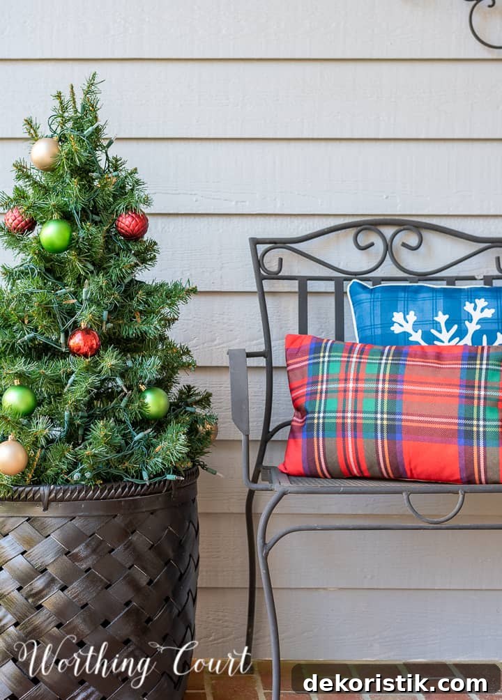 front porch decorated for Christmas with red and white garland, planters, trees, lanterns, rugs and pillows