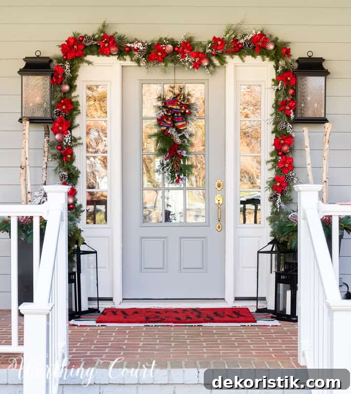 front porch decorated for Christmas with red and white garland, planters, trees, lanterns, rugs and pillows