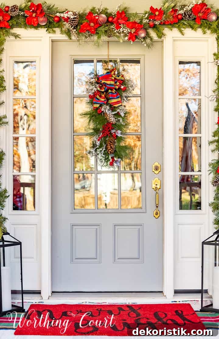 front porch decorated for Christmas with red and white garland, planters, trees, lanterns, rugs and pillows