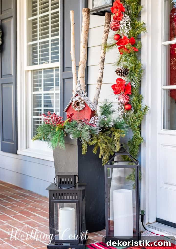 front porch decorated for Christmas with red and white garland, planters, trees, lanterns, rugs and pillows