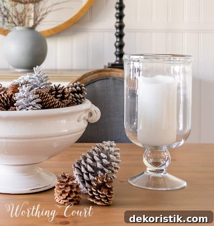 white pedestal bowl filled with pinecones and glass candle holders on wood dining table