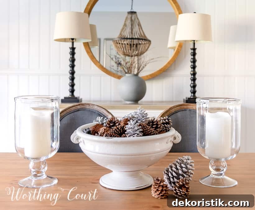 white pedestal bowl filled with pinecones and glass candle holders on wood dining table