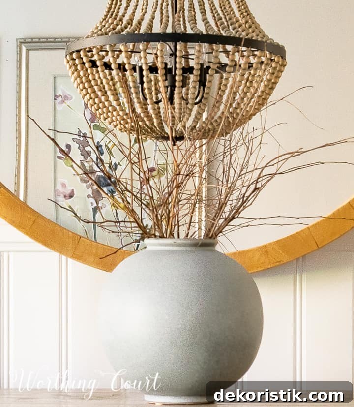 gray vase filled with bare branches in front of round mirror on sideboard