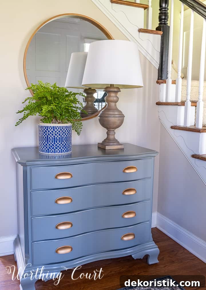 round mirror above a gray chest with lamp and planter