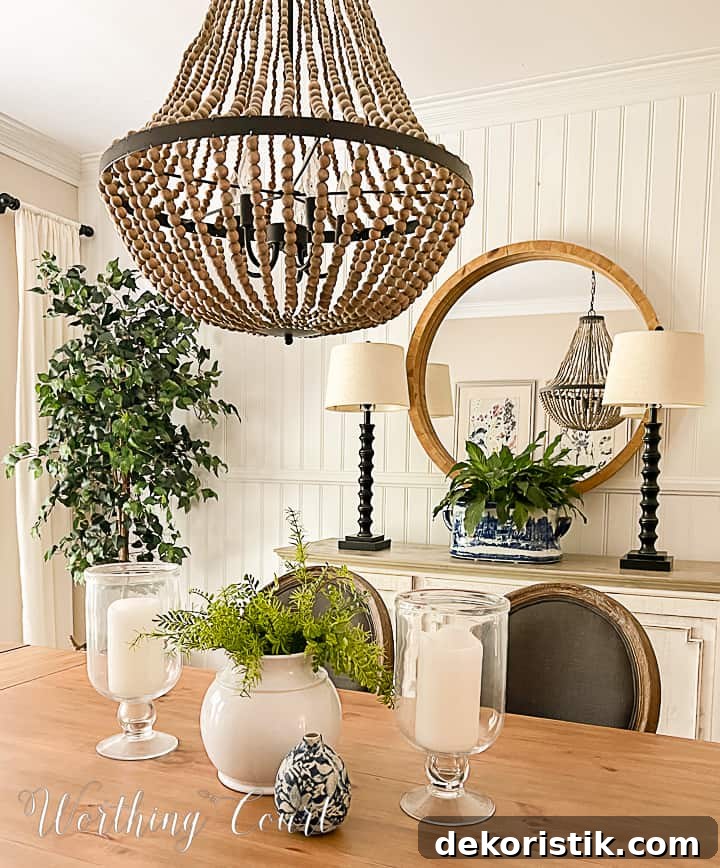 Summer decorations in a dining room consisting of a pretty blue and white urn on the sideboard and a faux plant with large glass hurricane lanterns for the table centerpiece. The type of urn on the sideboard is actually called a footbath and looks just gorgeous filled with a large peace lily