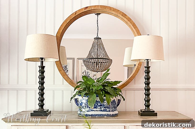 Dining room sideboard with round mirror, buffet lamps and blue and white urn filled with a plant