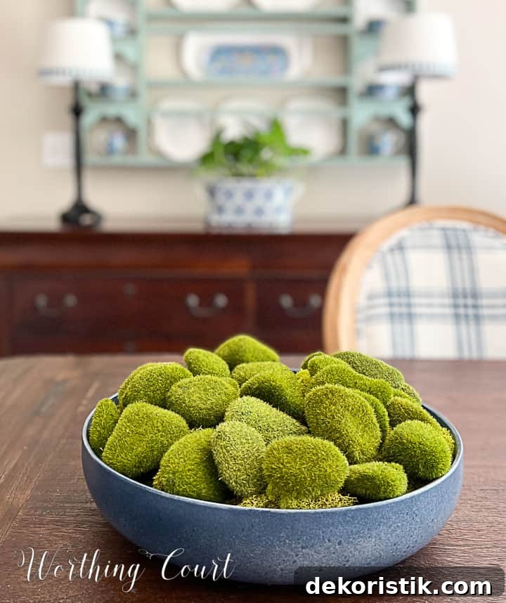 blue bowl filled with artificial moss covered rocks on a dining table with a plate rack in the background