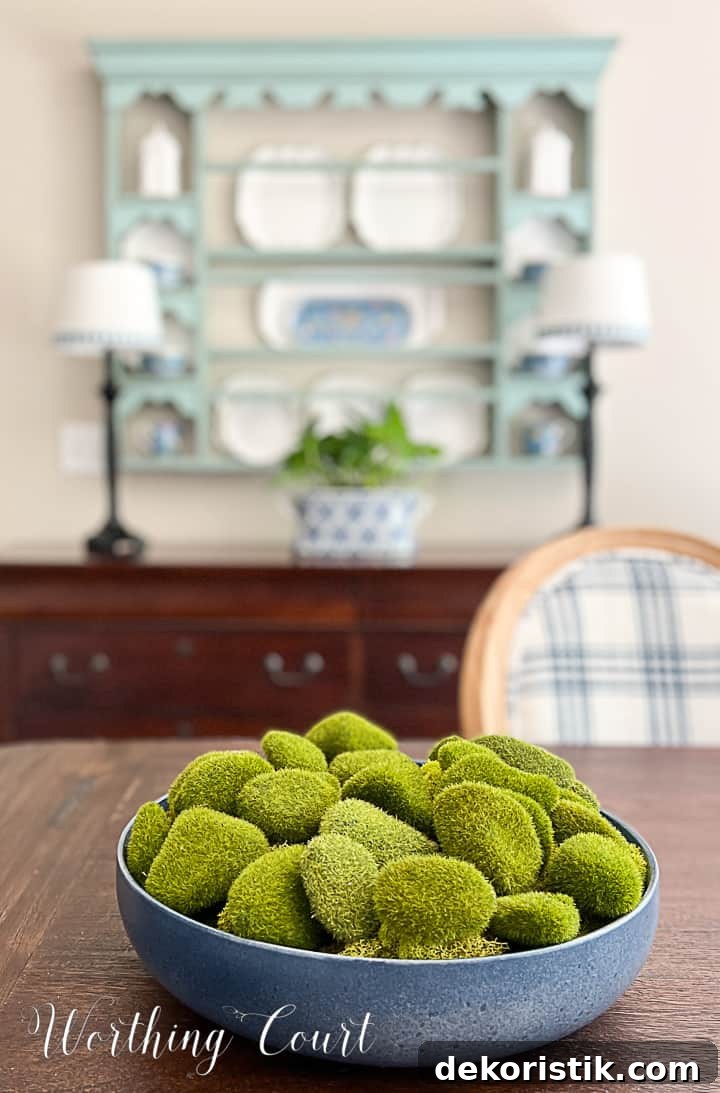 blue bowl filled with artificial moss covered rocks on a dining table with a plate rack in the background
