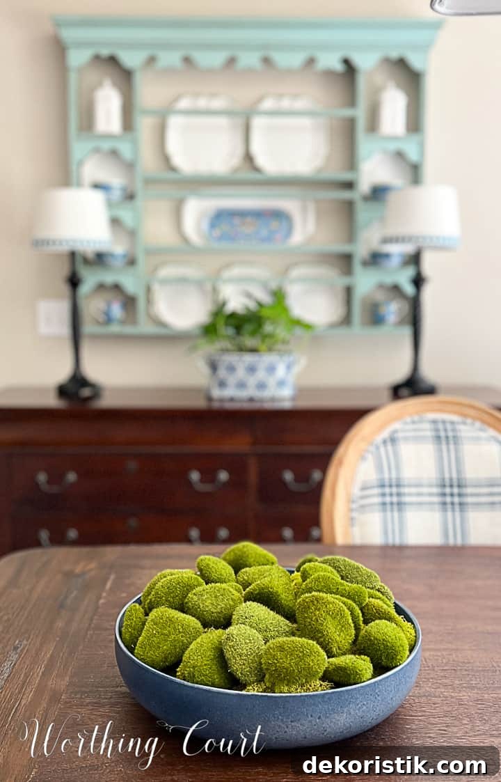 blue bowl filled with artificial moss covered rocks on a dining table with a plate rack in the background