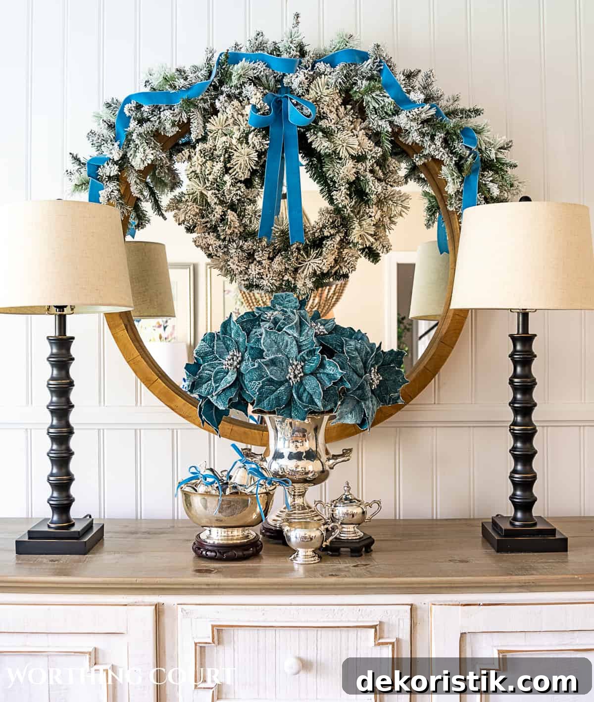 Sterling silver champagne bucket and Paul Revere bowl with French blue Christmas decorations in front of a round mirror above a sideboard