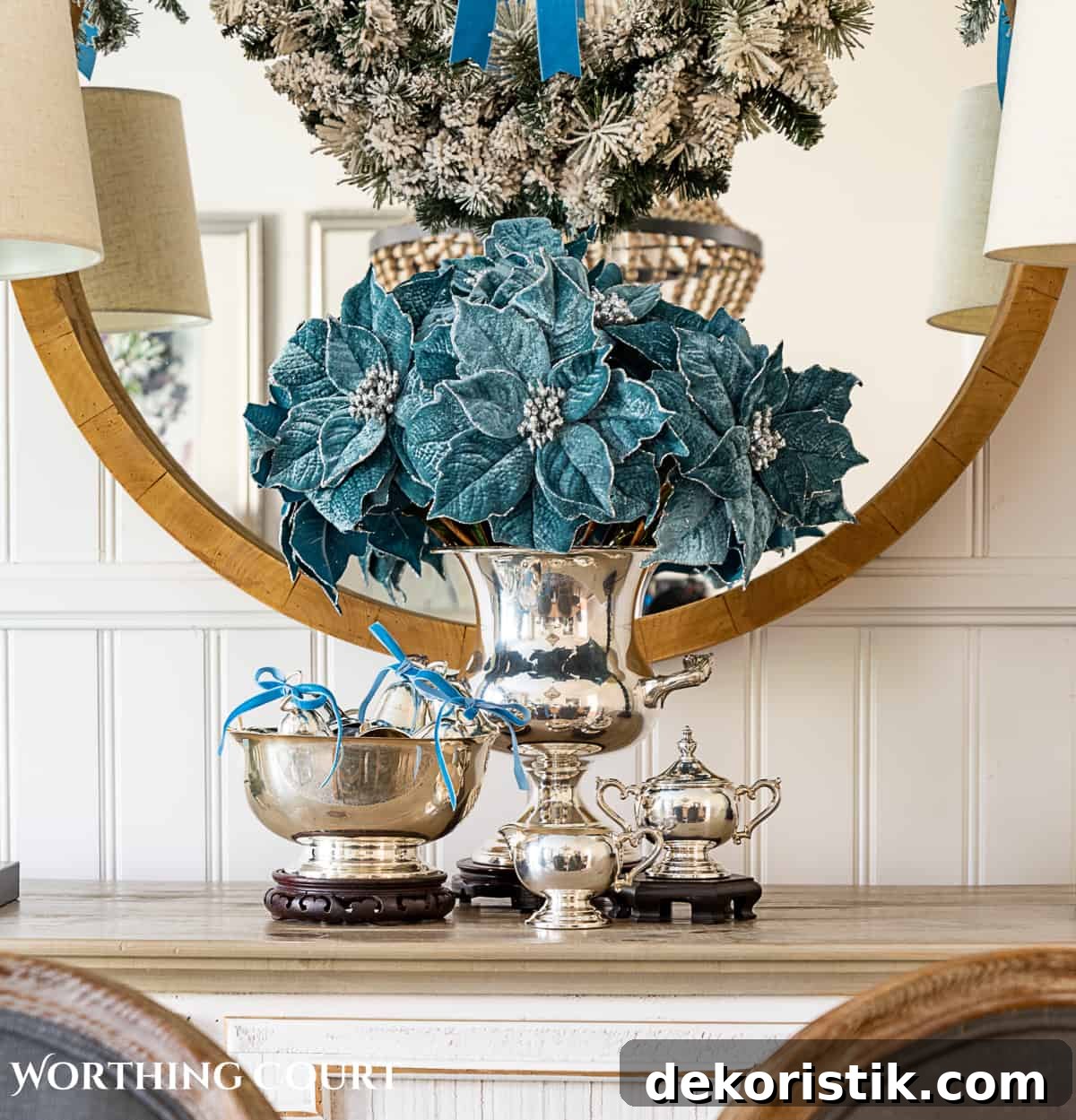 Sterling silver champagne bucket and Paul Revere bowl with French blue Christmas decorations in front of a round mirror above a sideboard