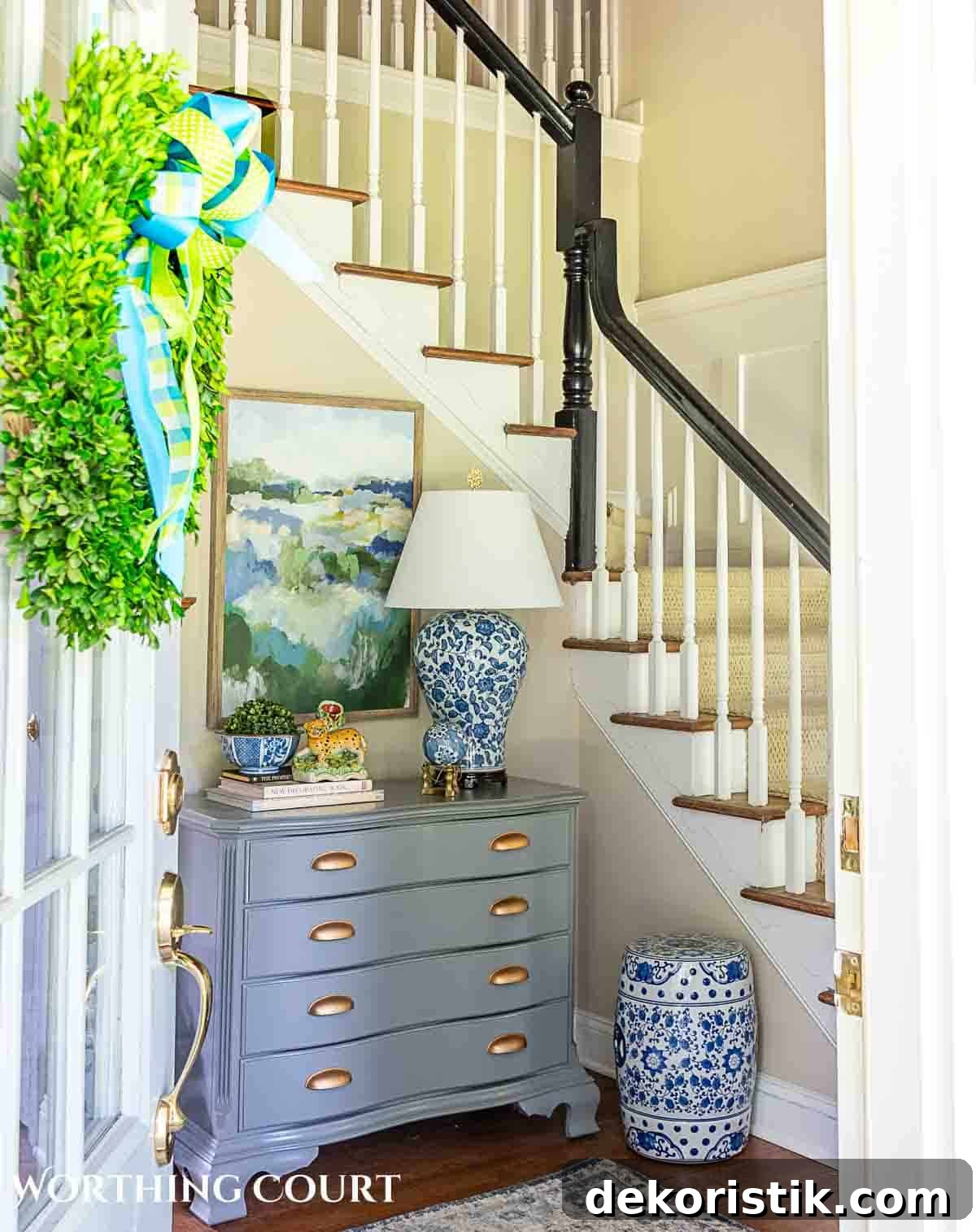 view through front door of a foyer decorated for summer included a gray chest, abstract art and blue and white accessories.