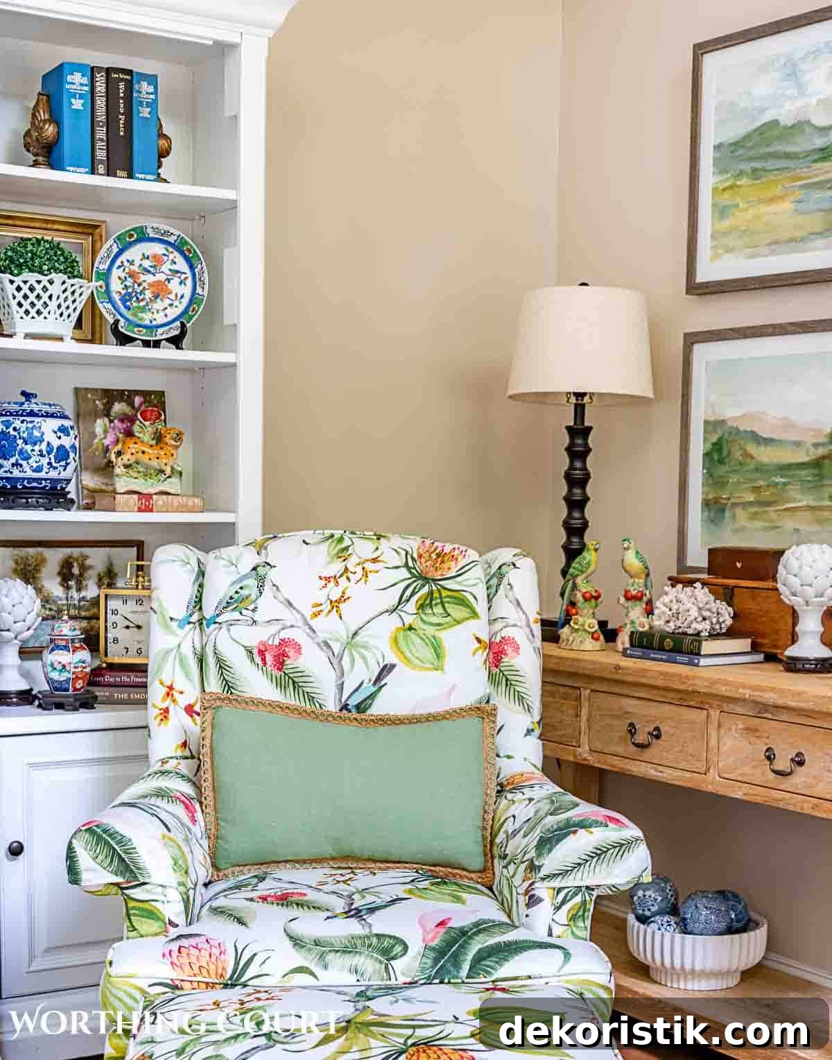 floral upholstered arm chair with green pillow in front of shelves and console table with summer decorations