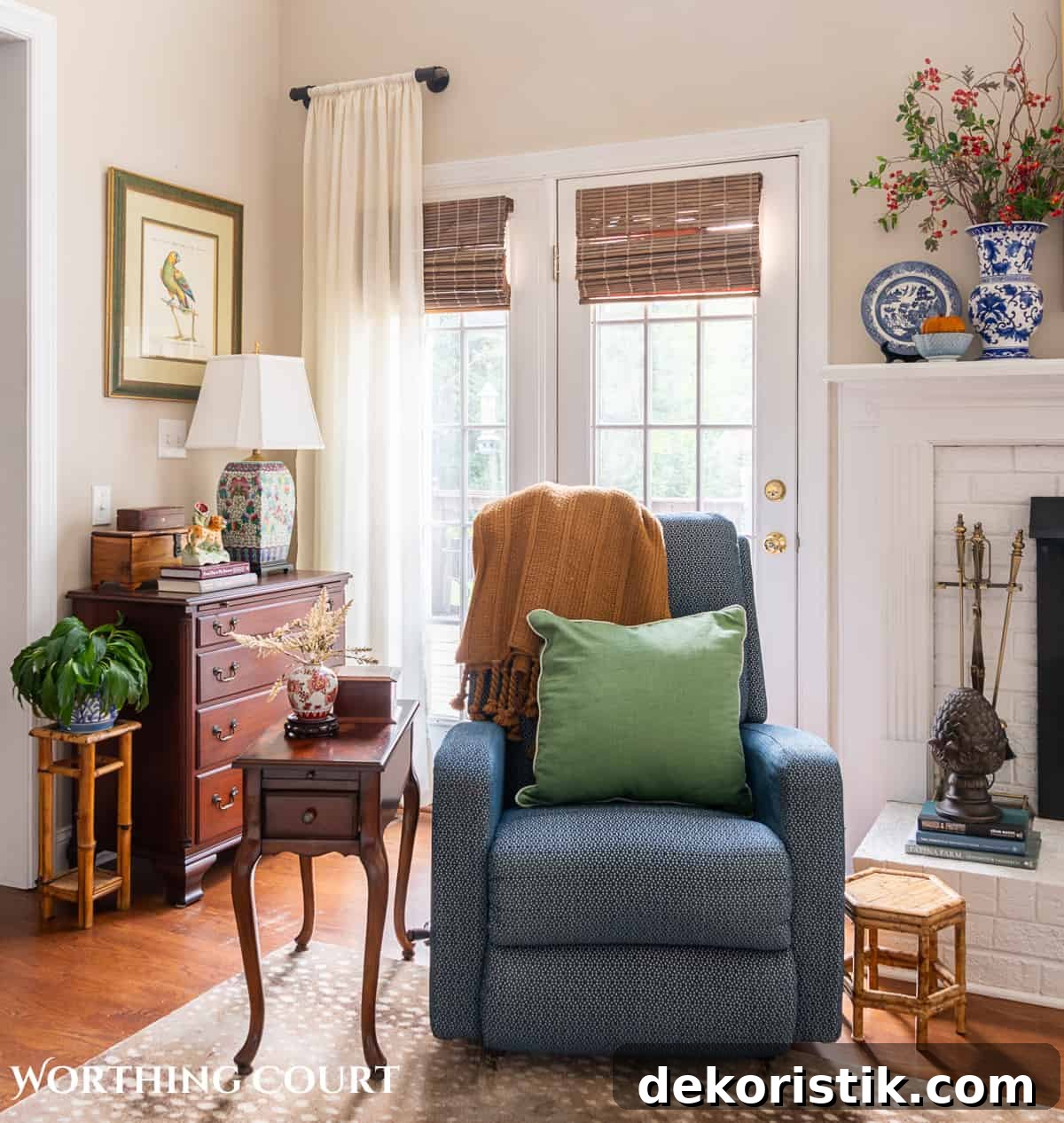 blue arm chair in front on french doors beside small table and chest with lamp