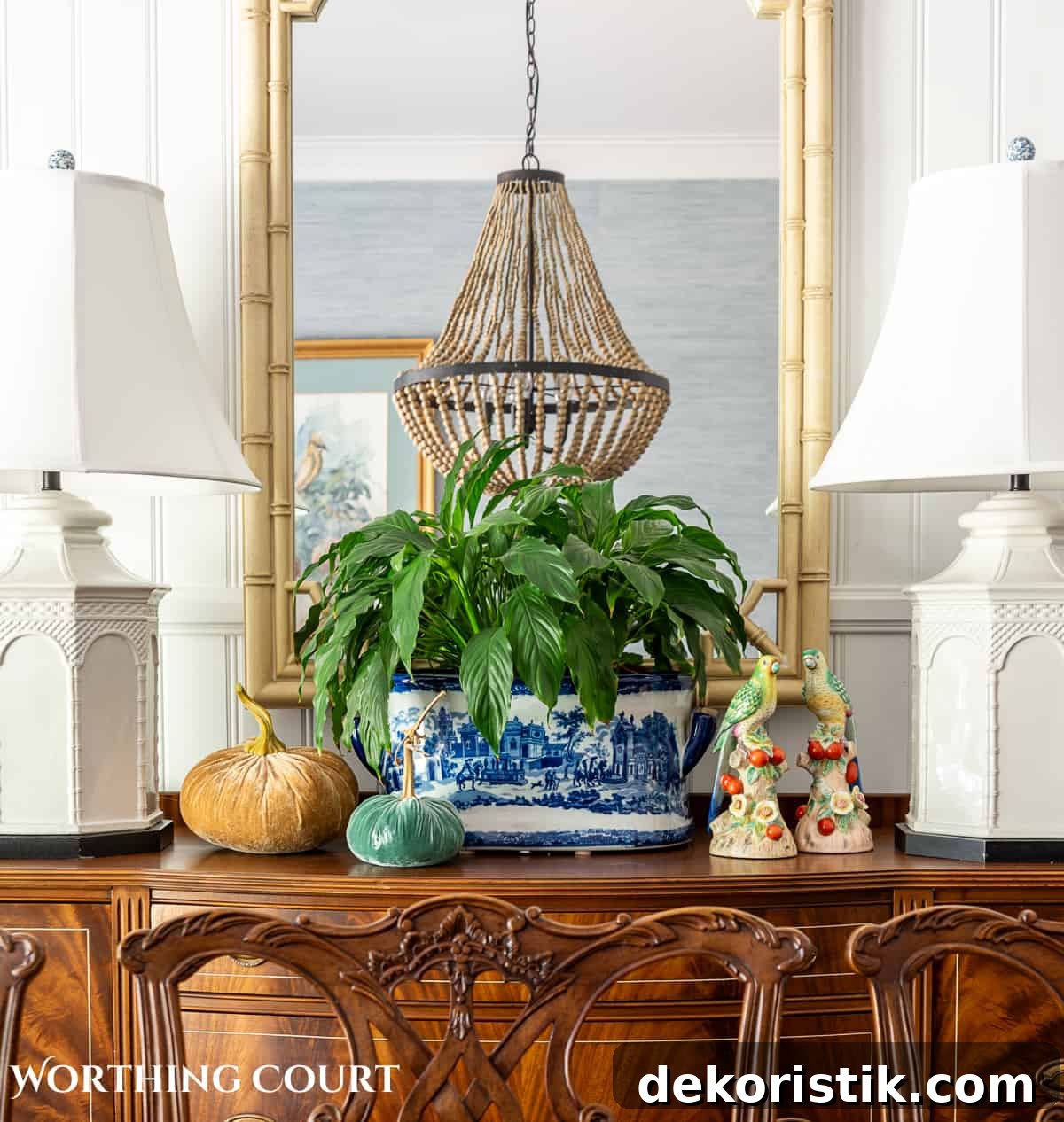 faux bamboo mirror hanging above a wood sideboard with two white lamps and fall decorations