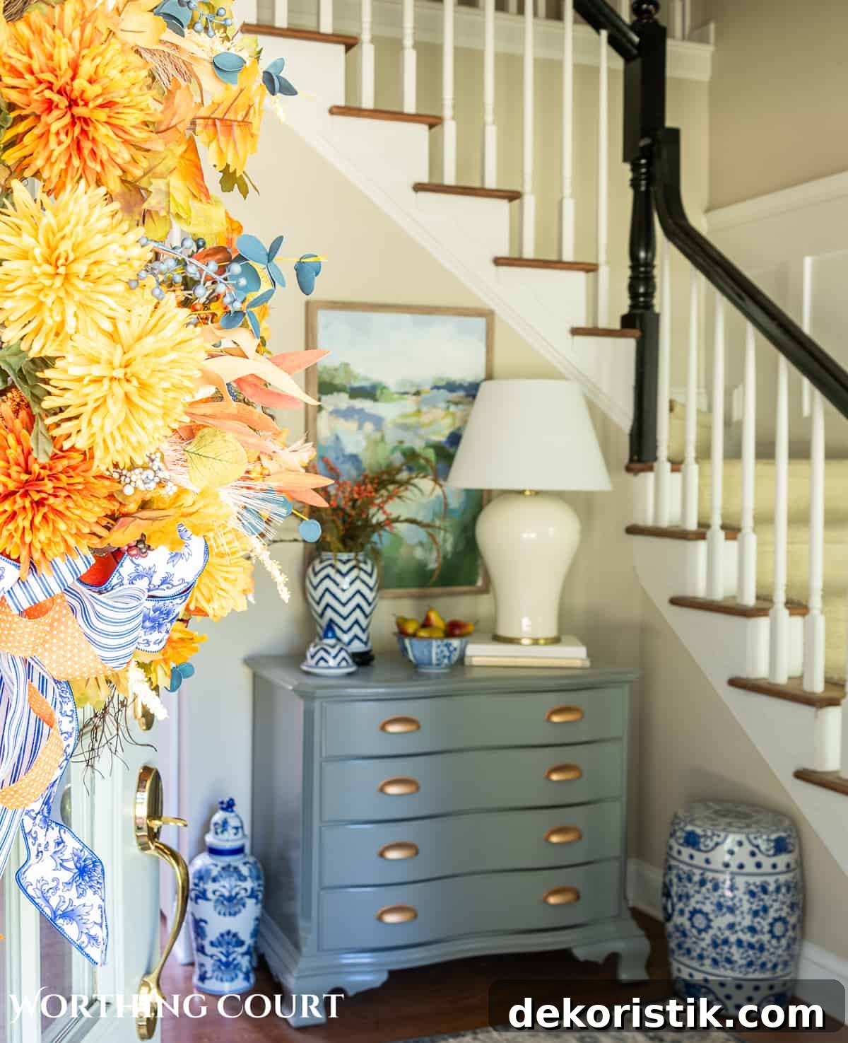 blue and white ginger jar with faux fall stems and a bowl of fake pears beside a white lamp on a gray chest