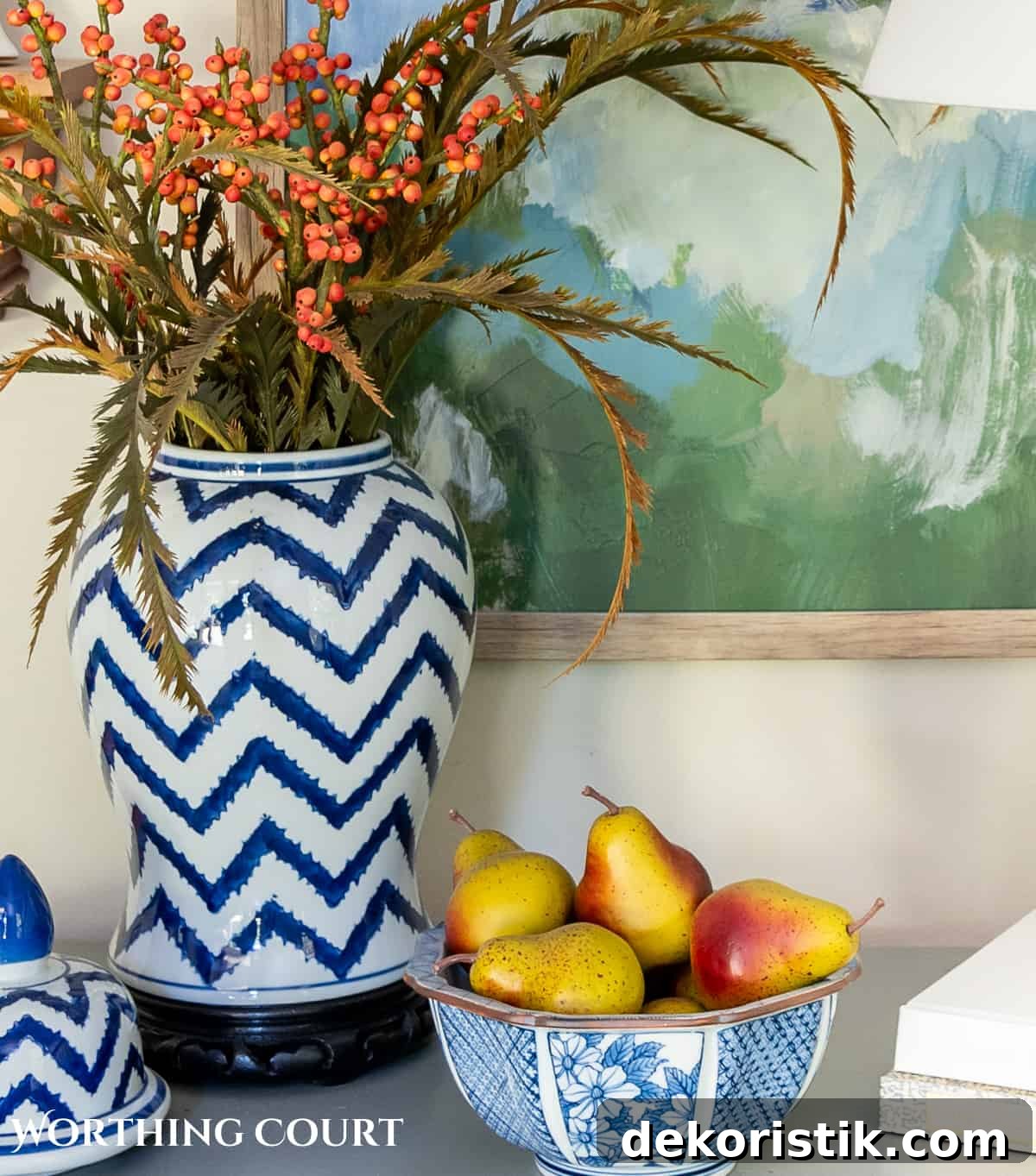 blue and white ginger jar with faux fall stems and a bowl of fake pears beside a white lamp on a gray chest