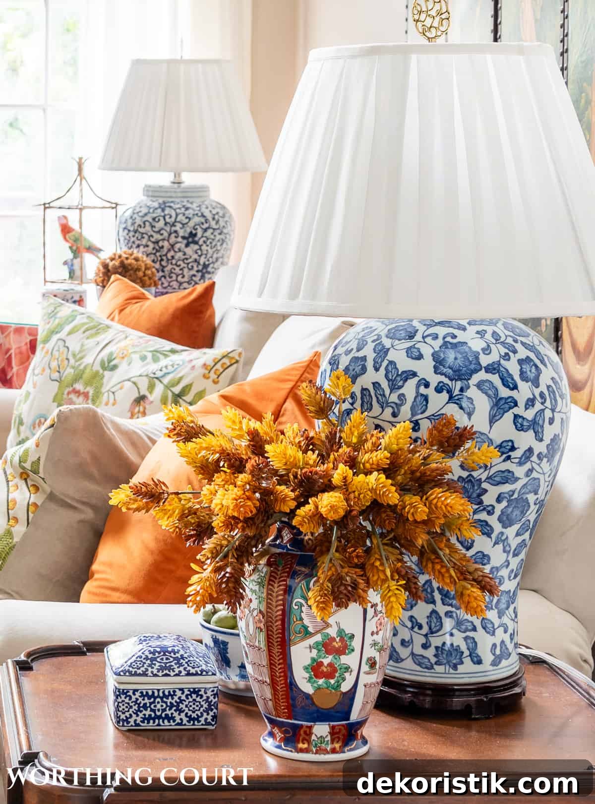 blue and white lamp and a vase filled with fall stems on a brown wood end table