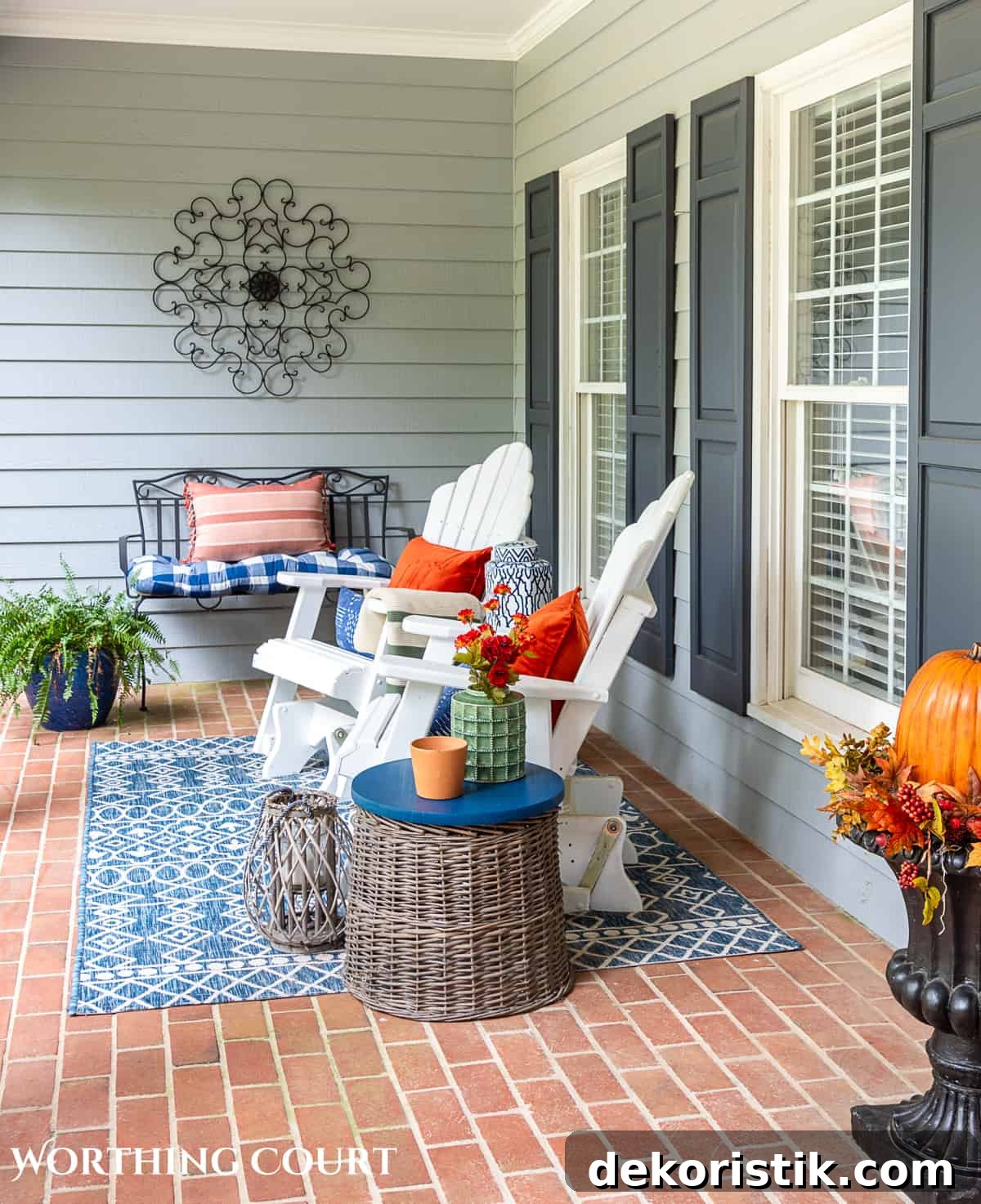 seating area on a large front porch decorated for fall with white gliders and other accessories