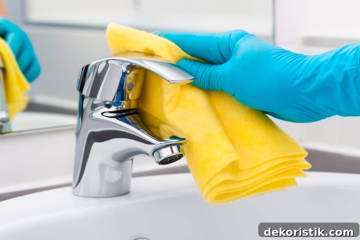 person's hand in a blue rubber glove cleaning a bathroom faucet
