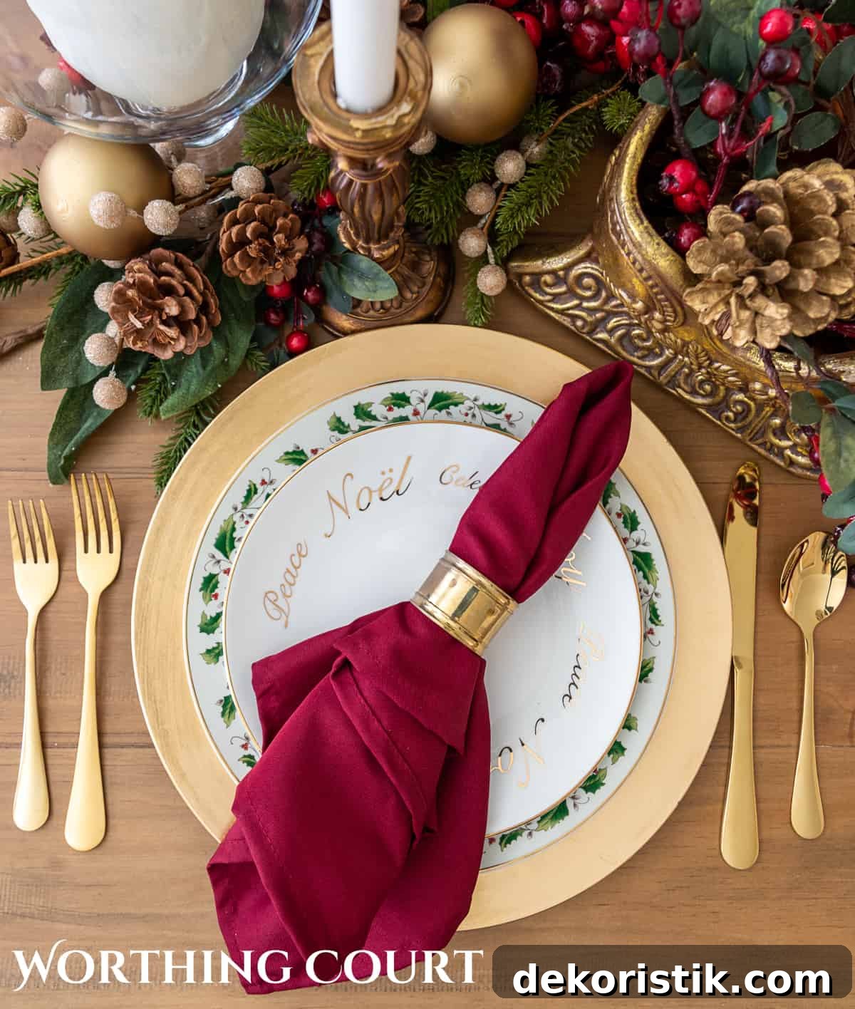 Christmas place setting with white plates stacked on a gold charger, with gold siverware and a burgundy napkin