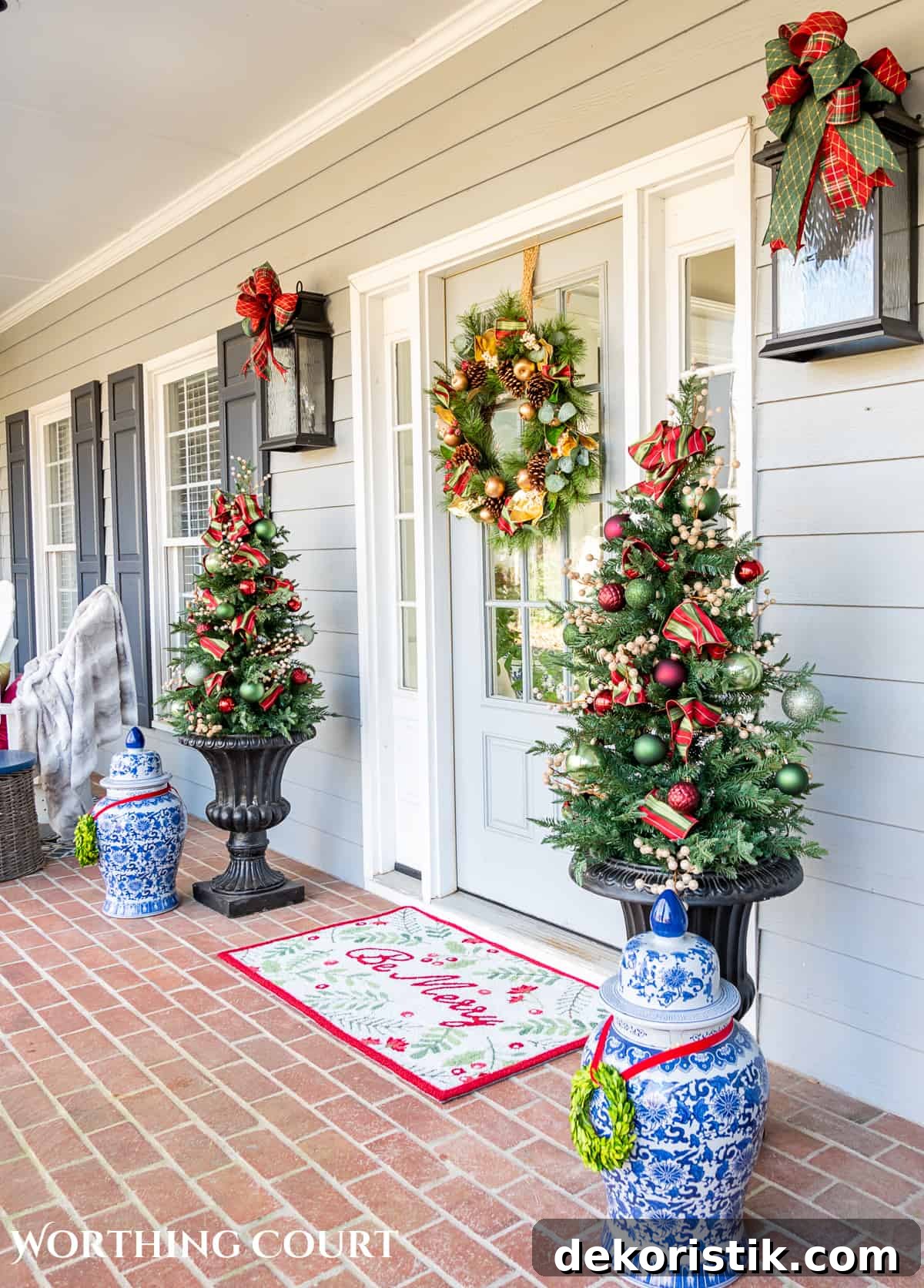front door with a Christmas wreath flanked by urns with small trees with red, green and gold Christmas decorations on them
