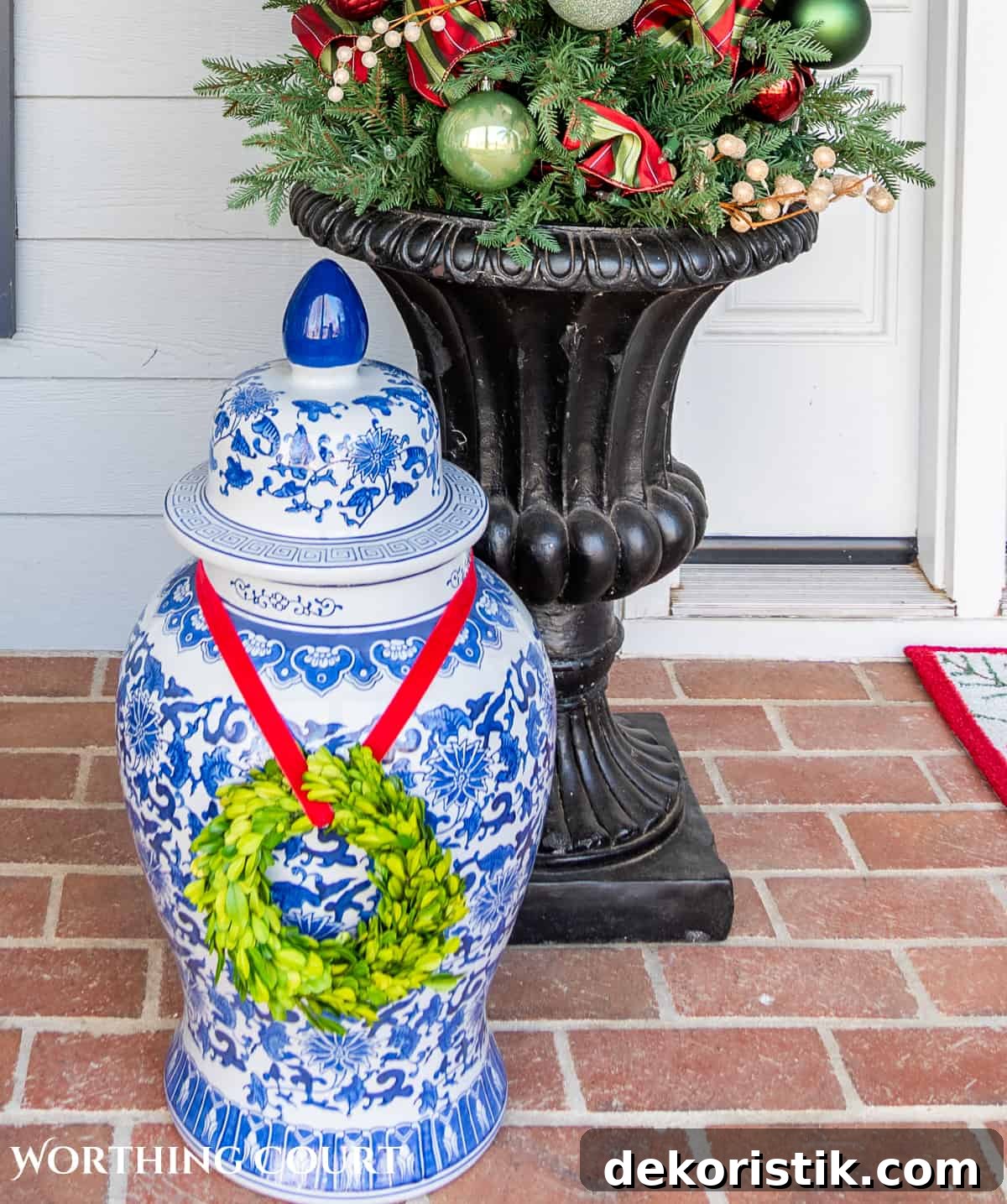 large blue and white ginger jar with a boxwood wreath around it in front of a planter on a front porch decorated for Christmas