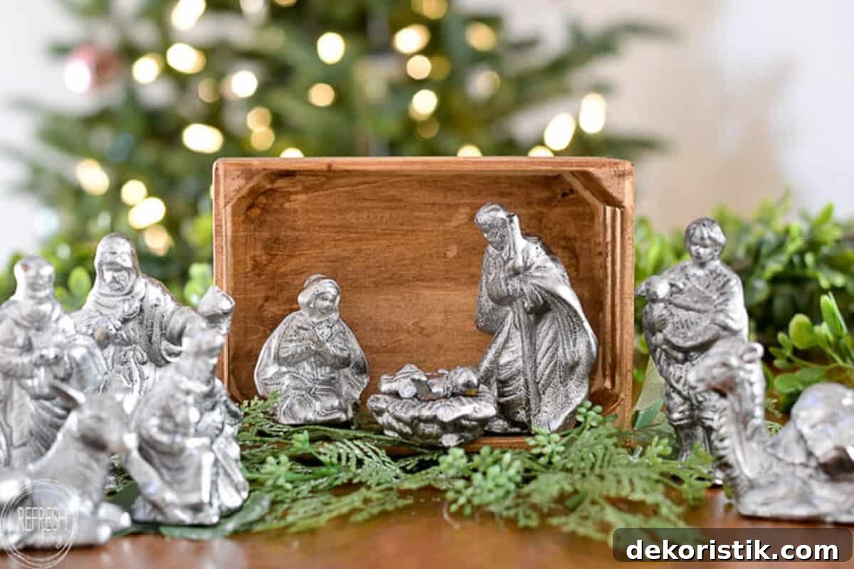 nativity scene display with silver figurines in a wood box surrounded by faux greenery