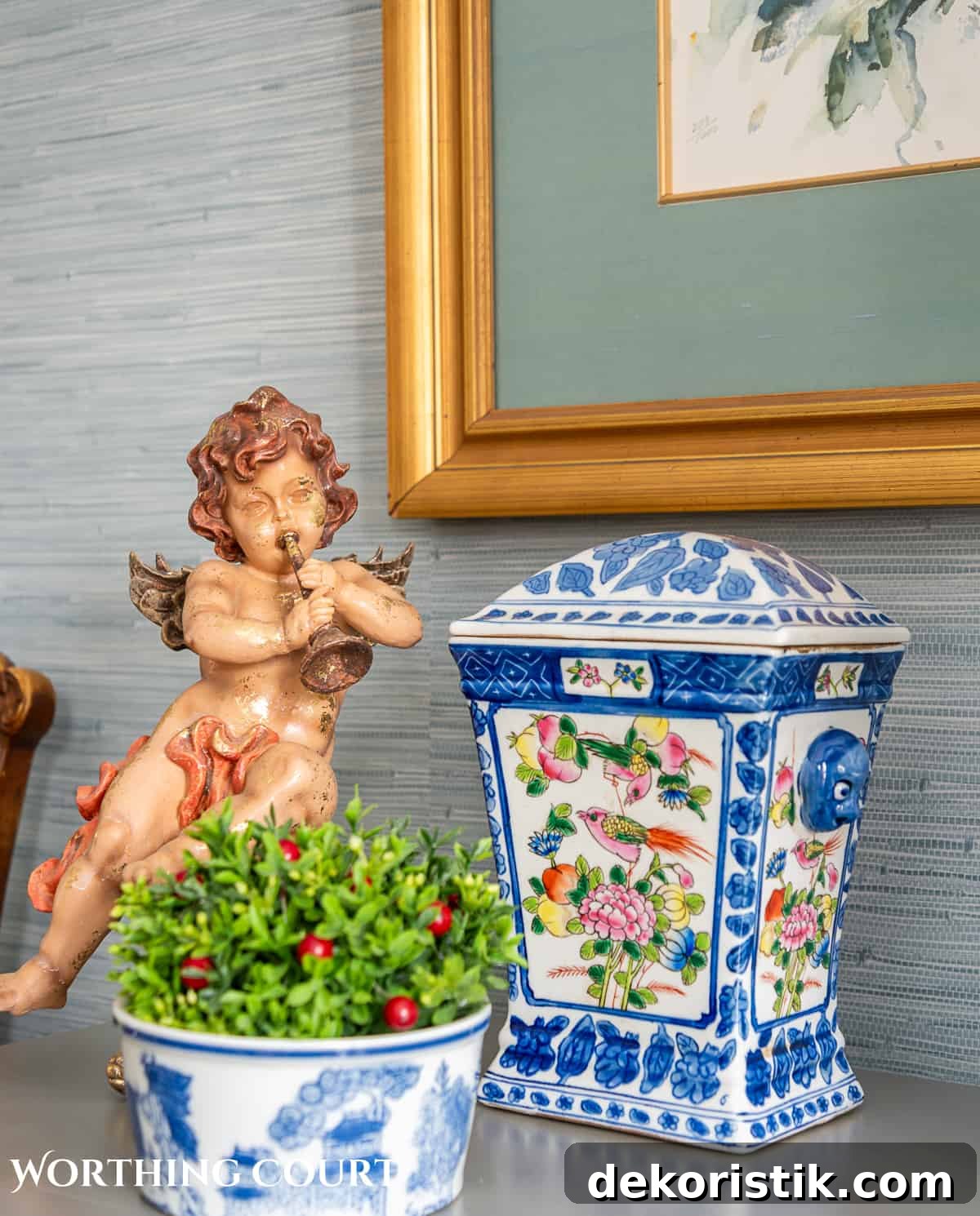 Vignette on a gray chest with a vintage cherub, blue and white urn and bowl with a boxwood orb with red berries