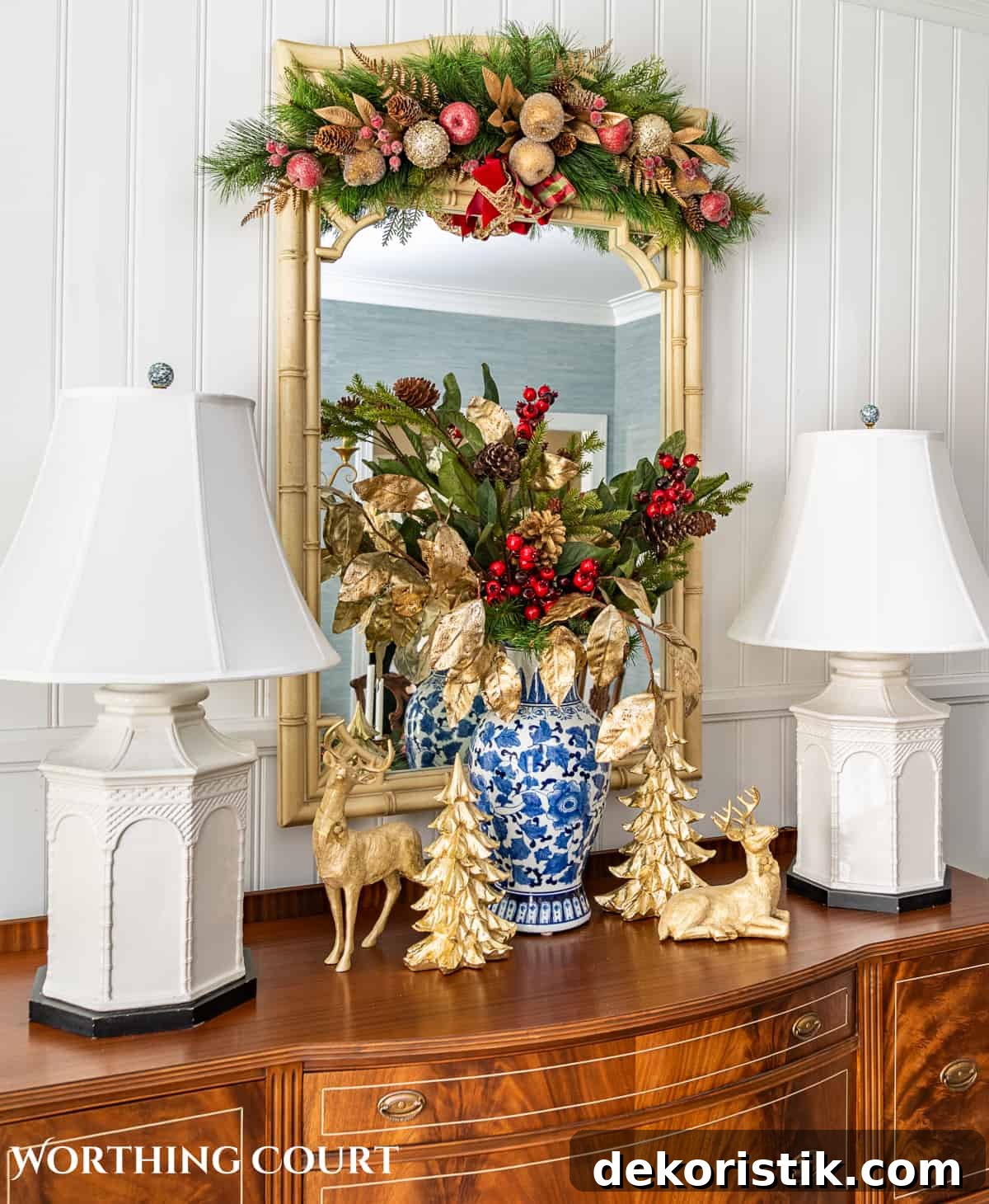 Christmas vignette on a sideboard with burgundy and gold stems in a blue and white vase flanked by gold deer and gold Christmas trees