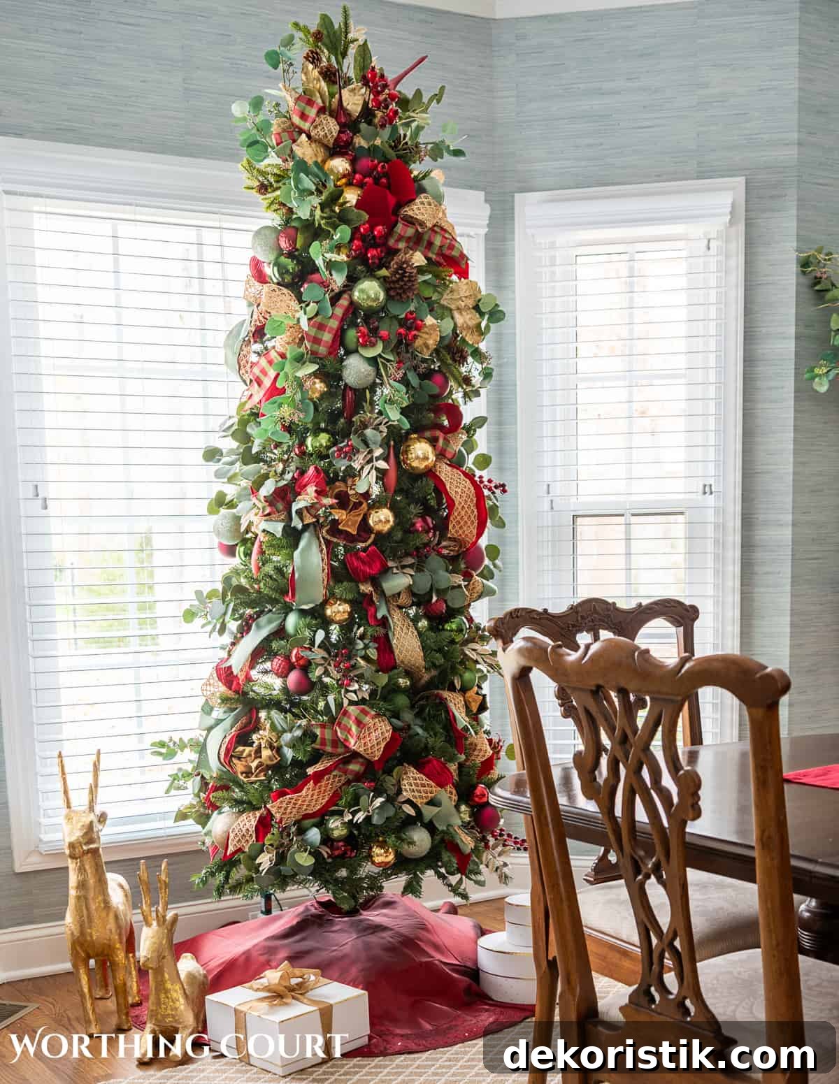 Slim Christmas tree with burgundy, green and gold decorations in a bay window.