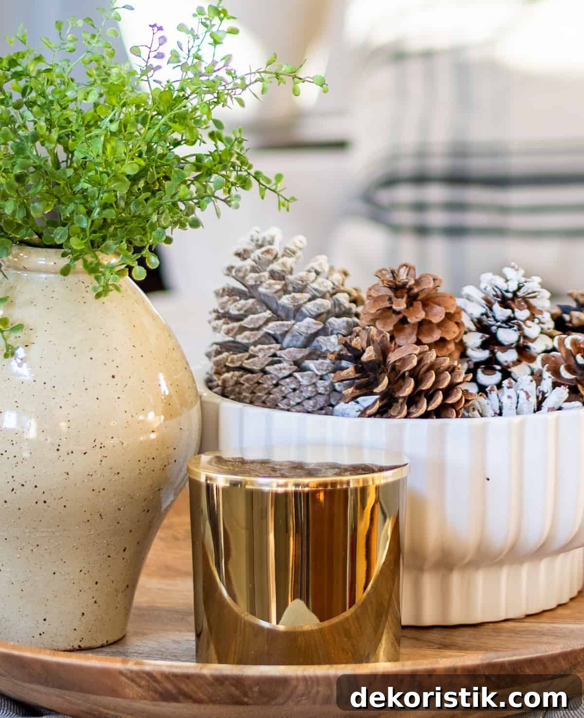 winter vignette with a white bowl, pinecones, candle and faux greenery in a vase