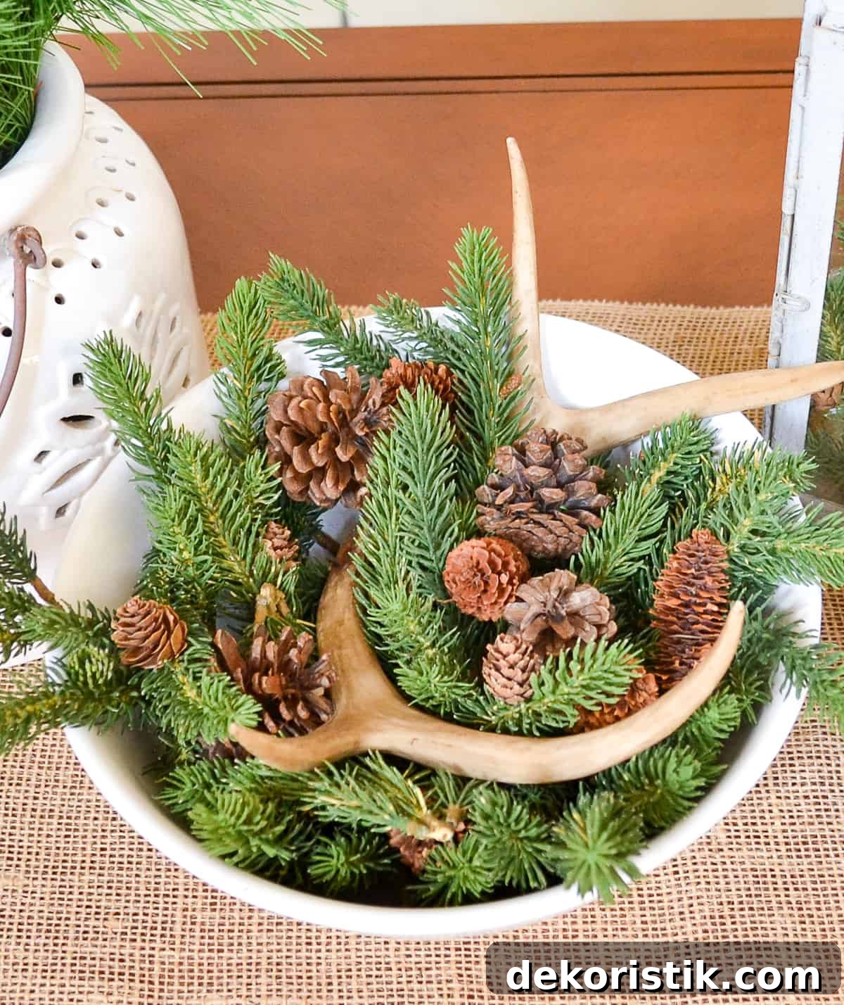 white bowl filled with faux greens, pinecones and faux antlers for winter decor