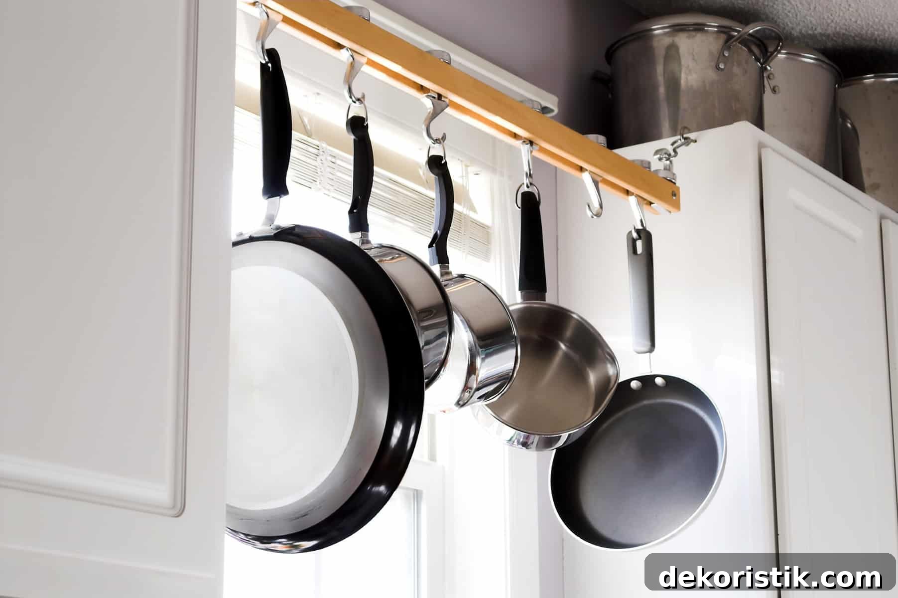 stainless steel cooking pans hanging in a window from hooks on a wooden rod