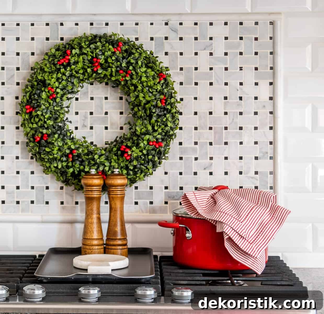 Christmas wreath on backsplash above cooktop with red dutch oven, red and white striped kitchen towel and wood salt and pepper mills