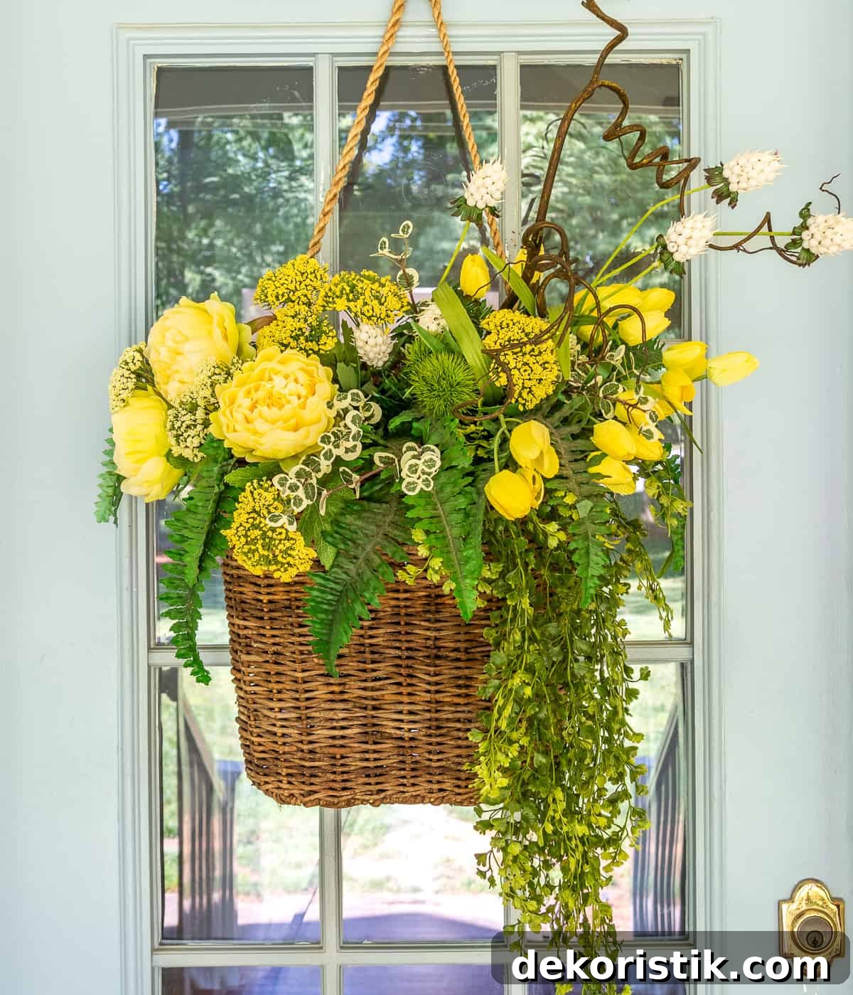 yellow flowers and greenery in a hanging basket on a gray front door for a spring door decoration