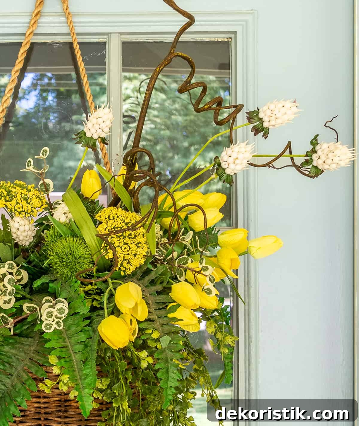 yellow flowers and greenery in a hanging basket on a gray front door for a spring door decoration