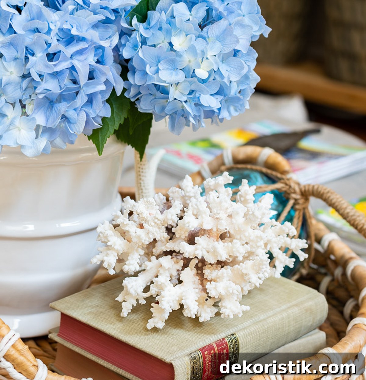 a piece of white coral on top of a stack of books beside a white vase filled with blue hydrangeas