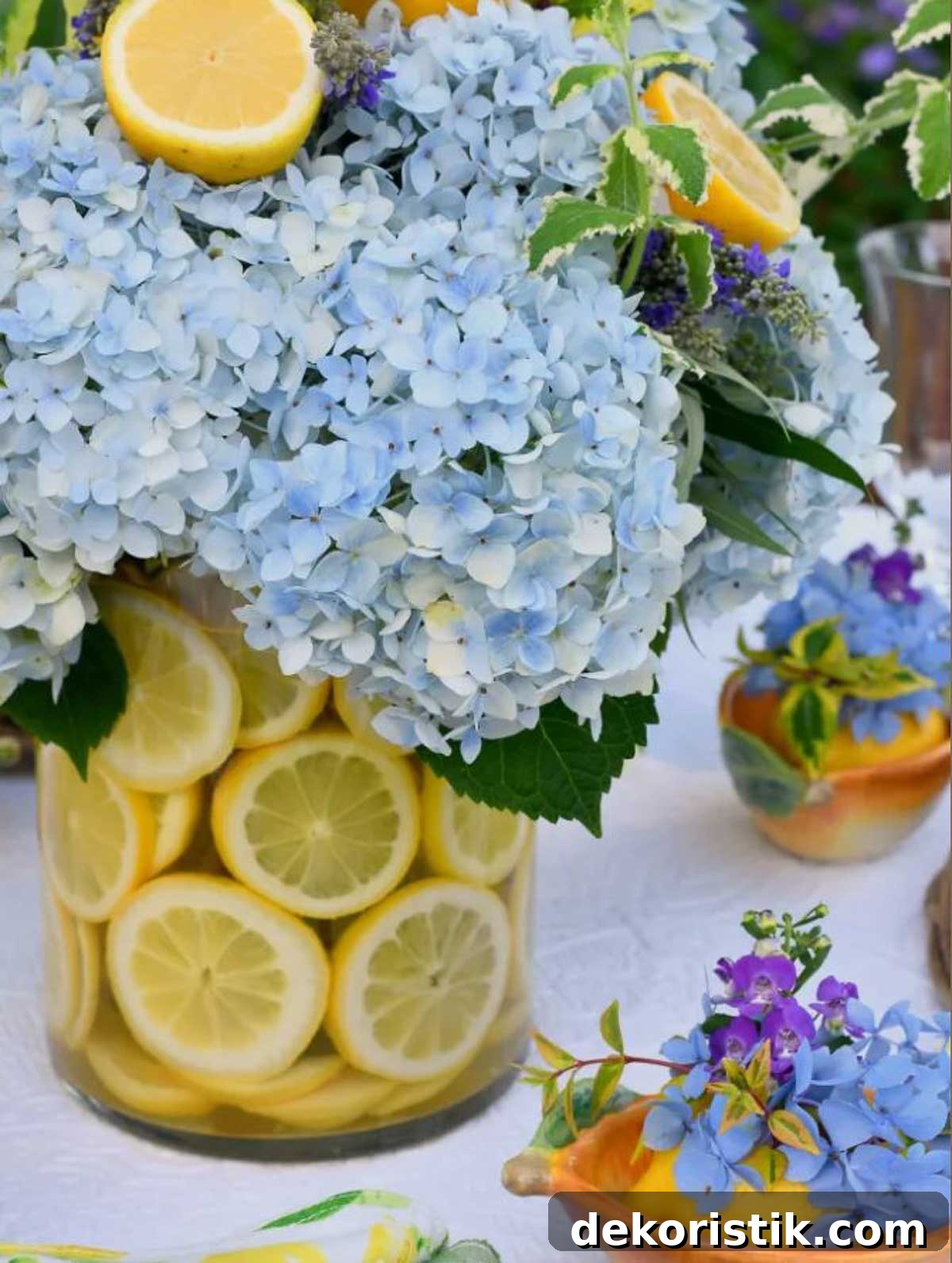 clear glass vase with sliced lemons around the side and an arrangement of blue hydrangeas