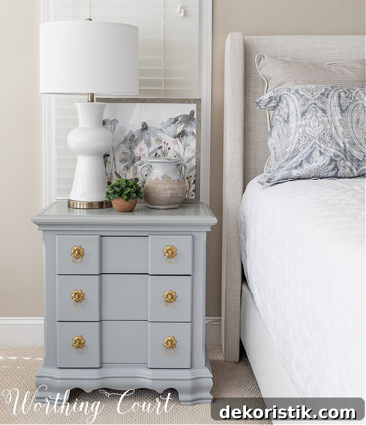gray nightstand with a white lamp beside a bed with an upholstered headboard