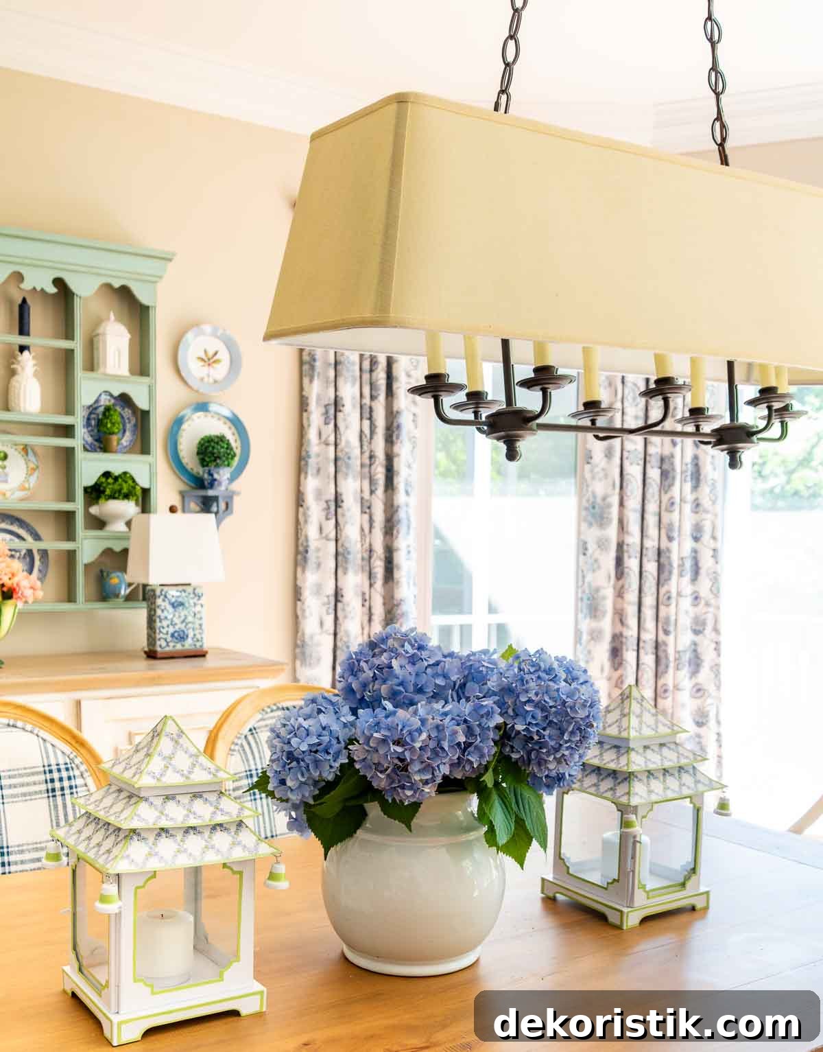 blue hydrangeas in a white vase flanked by pagoda style lanterns on a wood dining table